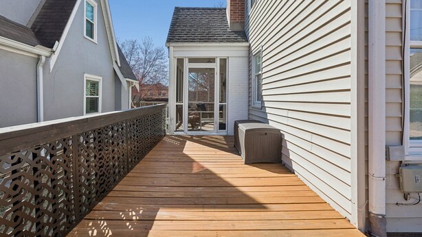Eine Holzdiele mit einer Glastür, die auf eine Terrasse führt, eine weiße Außenwand und ein Metallzaun.