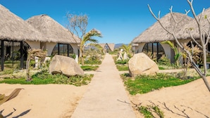 Un sendero que conduce a casas de campo con techo de paja, con grandes rocas y follaje a ambos lados.
