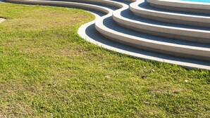 Un área ajardinada con piscina, césped y vista al océano.