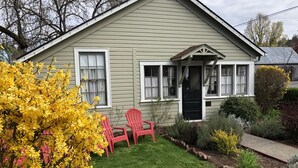 A house with a front porch, two red Adirondack chairs, a well-maintained lawn, and a variety of shrubs and plants.