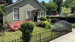 A single-story house with a front porch, a fenced yard, and red Adirondack chairs.