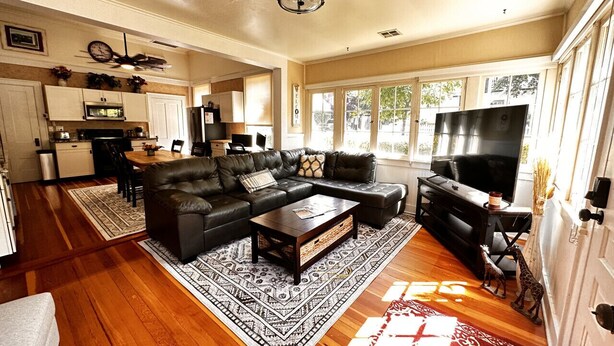 A spacious living room with a sectional sofa, a coffee table, and a TV. There is a kitchen area in the background.