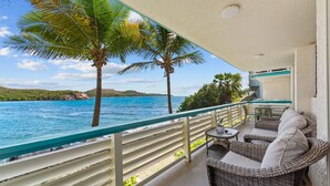 Un balcon avec des meubles en osier, une vue sur la mer et des palmiers.