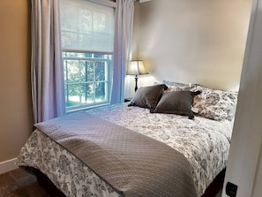 A bedroom with a large bed, a window with curtains, and a bedside lamp.