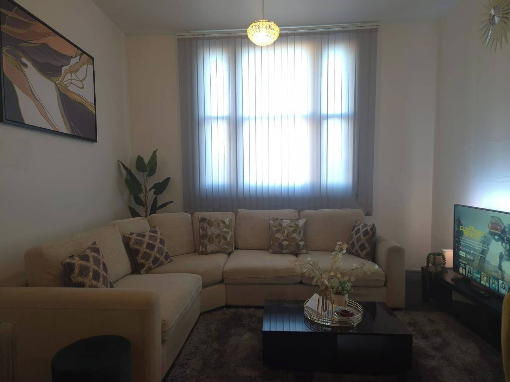 Een woonkamer met een beige hoekbank, een salontafel met een vaas en een televisie op een meubel.