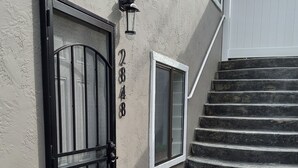 Ein Gebäudeeingang mit einem Metallgitter, einem kleinen Fenster und einer Treppe aus Stein, die zu einer weißen Tür führt.