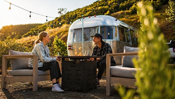 Deux personnes sont assises sur un banc à l’extérieur d’un camping-car, avec un foyer entre elles.