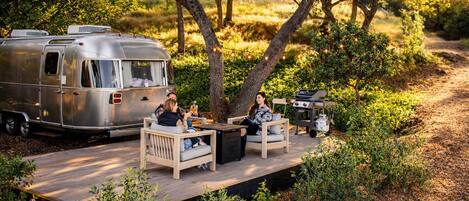 A recreational area with a trailer, outdoor seating, and a grill.