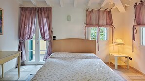 Um quarto com cama, mesa de cabeceira, luminária e janela com cortinas.