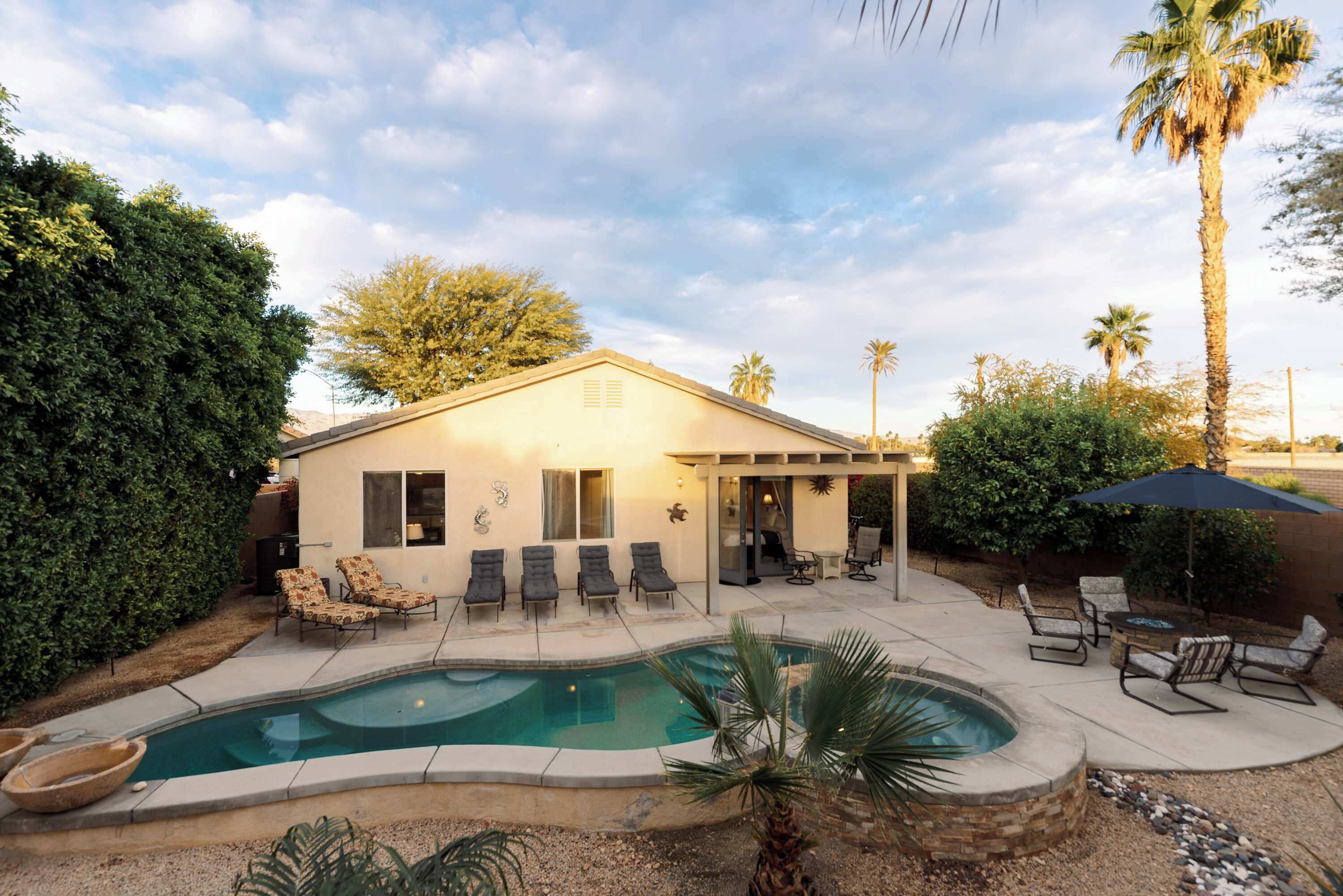 Une maison avec une piscine, un espace salon extérieur et des palmiers.
