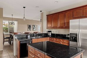 A modern kitchen with wooden cabinets, a stainless steel refrigerator, and a granite countertop. - Blue Jay by Nest Villas | Idyllic Pool & Spa (Indio)