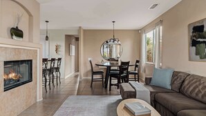 A living room with a fireplace, dining area, and a sofa. - Blue Jay by Nest Villas | Idyllic Pool & Spa (Indio)