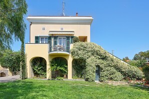 A two-story building with a balcony, arched entrance, and a well-maintained garden. - Casa Rossa Nel Giardino di Renzo with pool - Mareri apartments (Imperia)