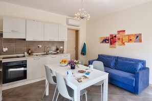 A modern kitchen with white cabinets, a dining table with chairs, a blue sofa, and wall art. - Levante - Mareri apartments (Imperia)