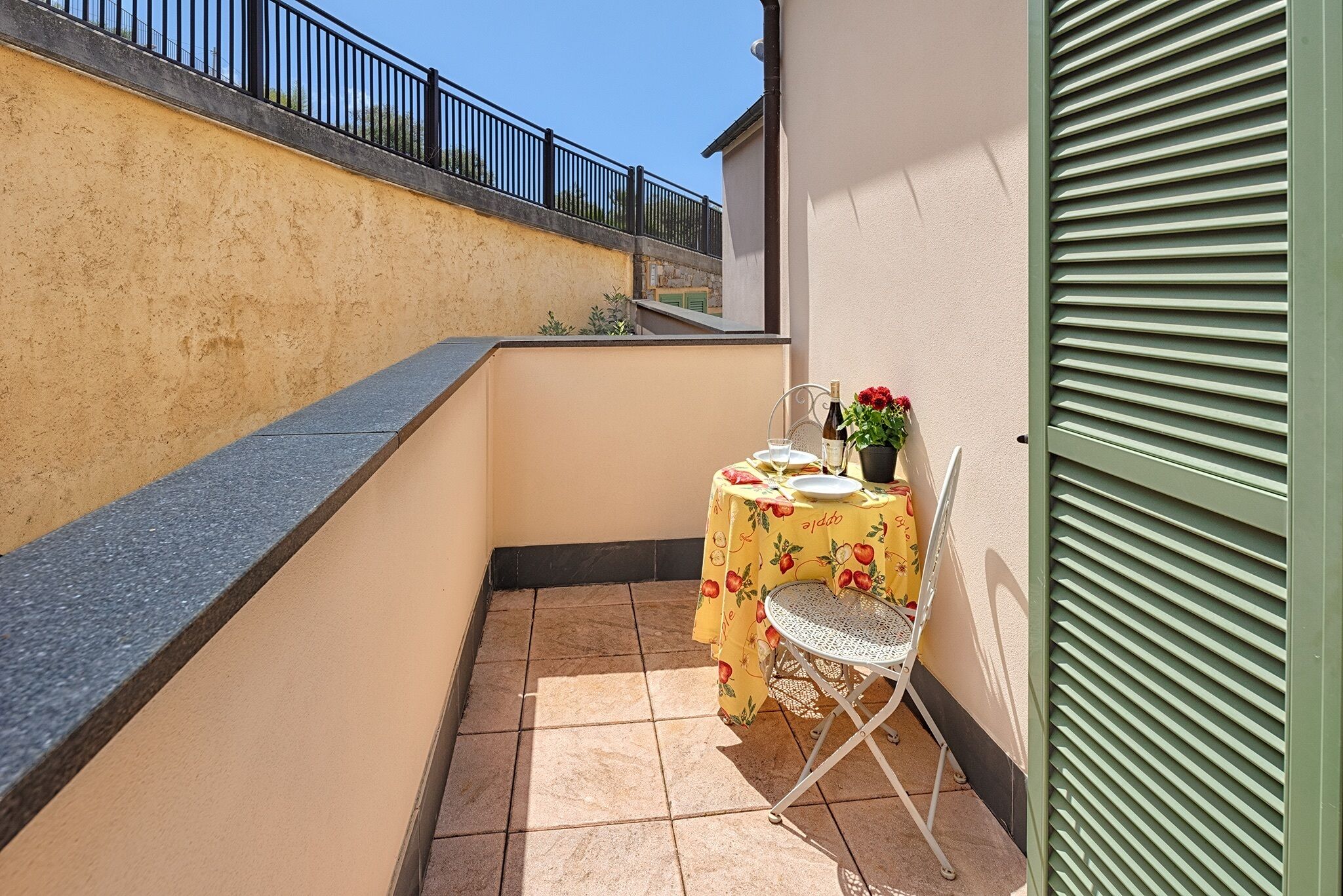 A small balcony with a table set for two, a chair, and a potted plant.