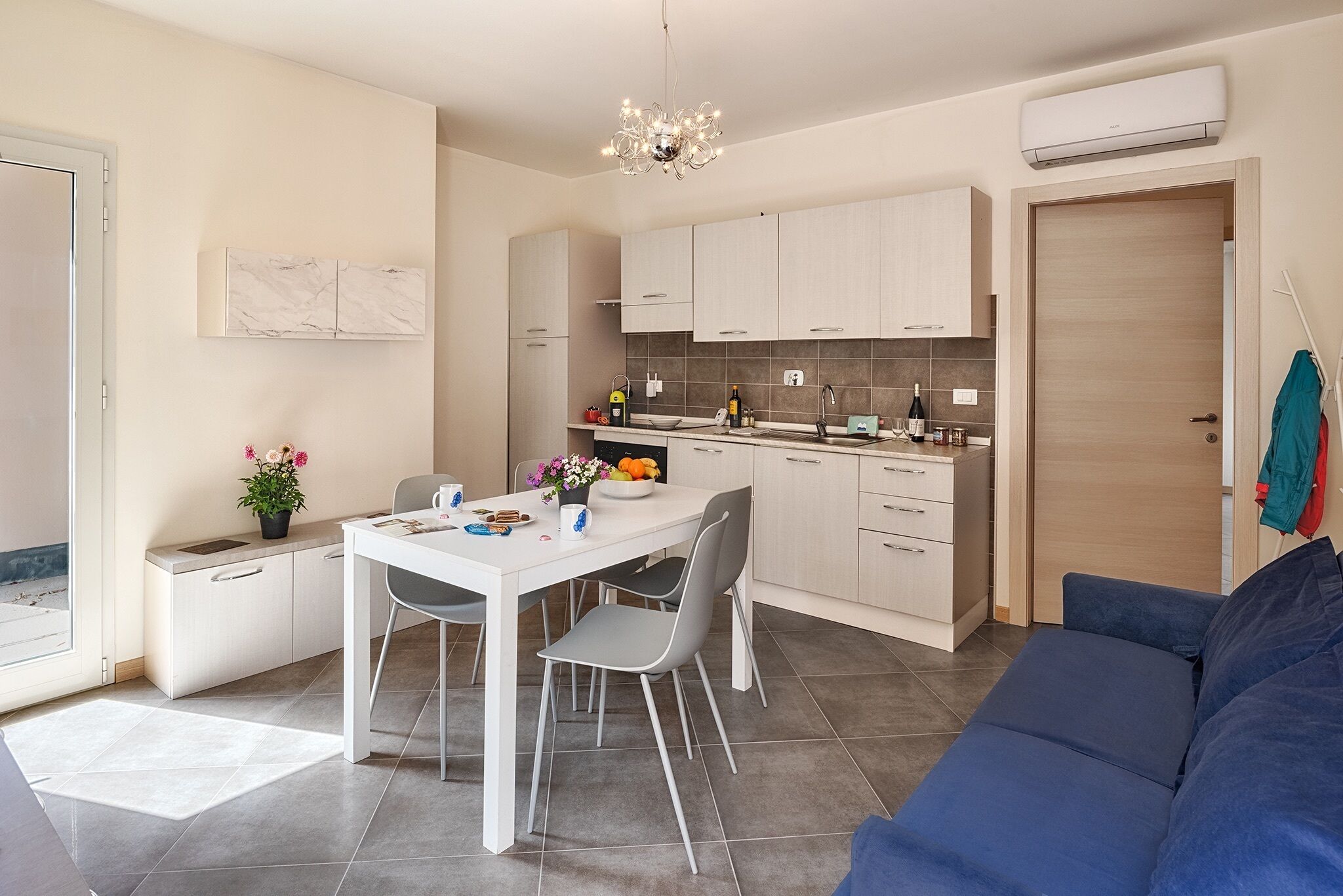Une cuisine moderne avec des meubles blancs, une table à manger et des chaises. On trouve un canapé bleu dans l’espace salon.