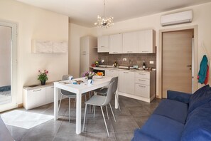A modern kitchen with white cabinets, a dining table, and chairs. There is a blue sofa in the living area. - Levante - Mareri apartments (Imperia)