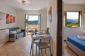 A modern living room with a dining area, a sofa, and a balcony with a view. - West - Mareri apartments (Imperia)
