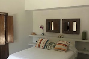A bedroom with a bed, two wall-mounted mirrors, a small shelf with decorative items, and a bedside table with a lamp.