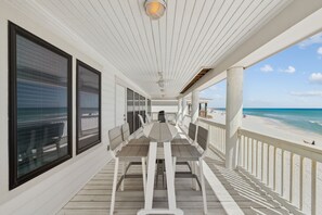 A covered outdoor deck with a table and chairs, overlooking a beach. - A Grand View – Stunning Gulf Views & Direct Beach Access (Santa Rosa Beach)