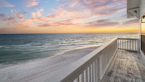 Eine Holzterrasse mit Blick auf einen Strand und einen Sonnenuntergang.
