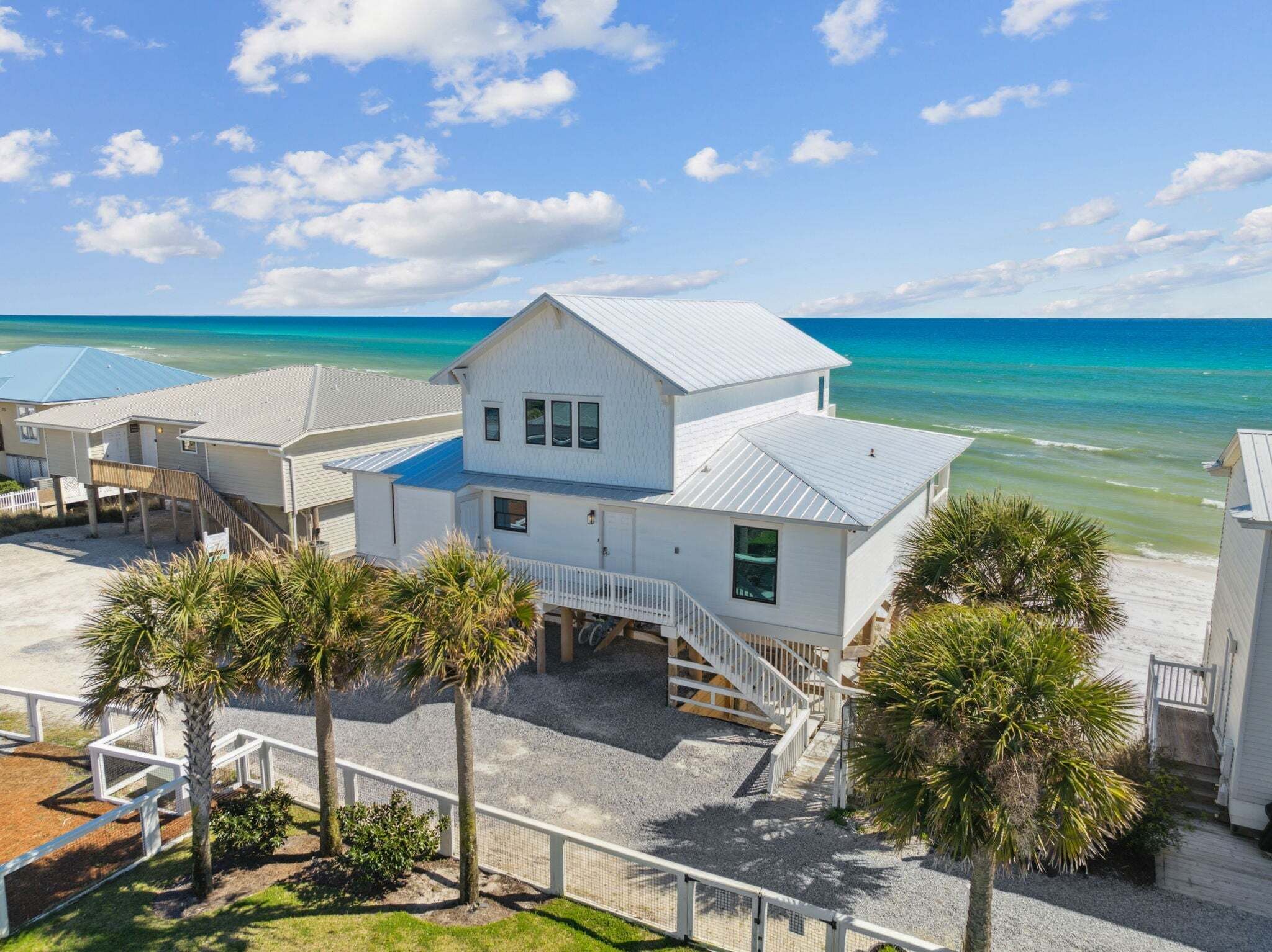 A beachfront property with a white house, a covered patio, and a view of the ocean.