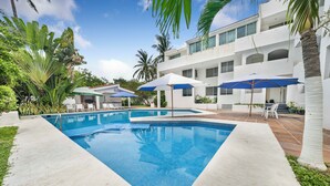 A swimming pool with a white tiled deck, surrounded by palm trees and a multi-story building with balconies. - CONDO OLA ALEGRE (Manzanillo)