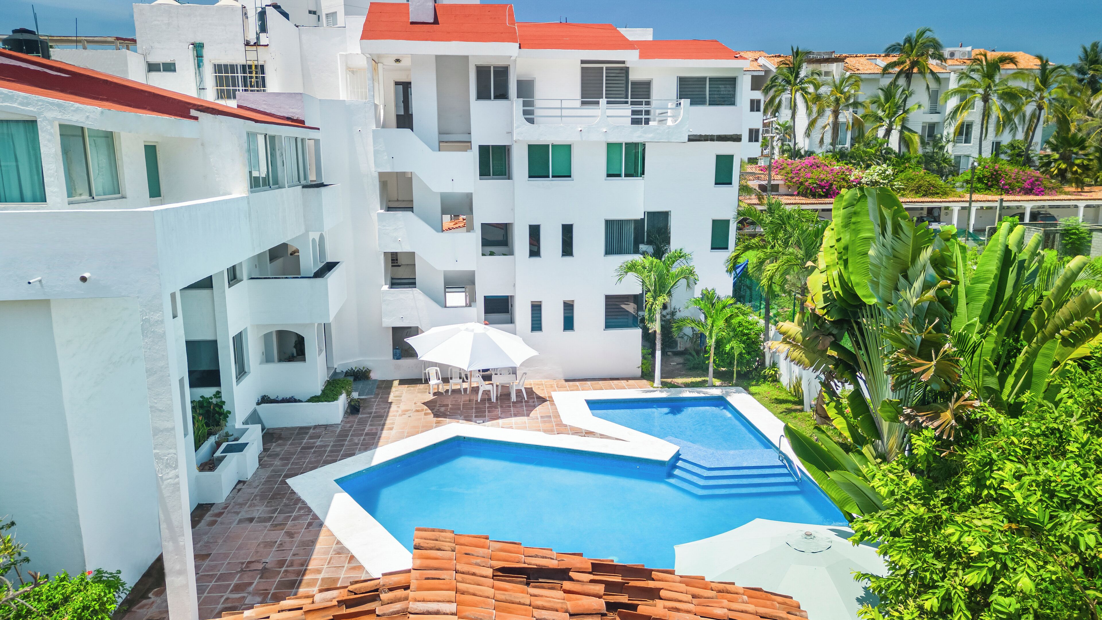Un edifici modern amb piscina, zona de seients a l'exterior i vegetació exuberanta.