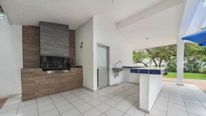 A modern outdoor kitchen with a built-in grill, a sink, and a door leading to a covered patio area. - CONDO OLA ALEGRE (Manzanillo)