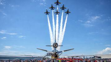 A large crowd gathered at an airshow with a central aircraft performing a stunt.