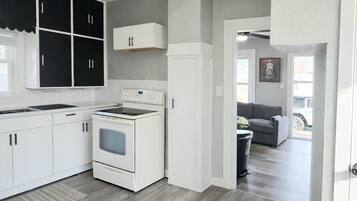 Een moderne keuken met witte kasten, een zwarte plafondventilator en een grijze vloer.