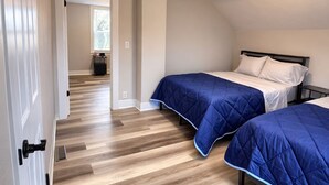 A bedroom with two beds, wooden flooring, and a white door.