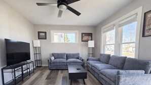 A modern living room with a flat-screen TV, two grey sofas, a coffee table, and a ceiling fan.