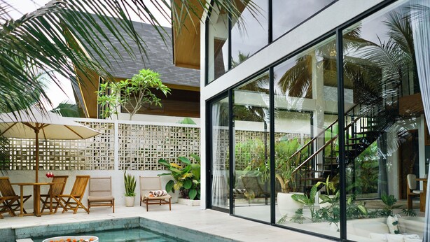 A modern outdoor pool area with a glass-enclosed staircase, lounge chairs, and potted plants. - Ubud Dzen Villas (Ubud)