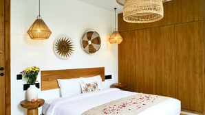 A neatly arranged bedroom with a wooden headboard, a large bed with white bedding, two wall-mounted lights, and a woven pendant light above the bed. - Ubud Dzen Villas (Ubud)