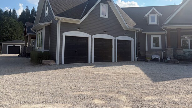 A residential house with a gravel driveway, two garage doors, and a stone pillar. - Newly renovated 1 Bedroom apartment in Alton, Ontario (Alton)