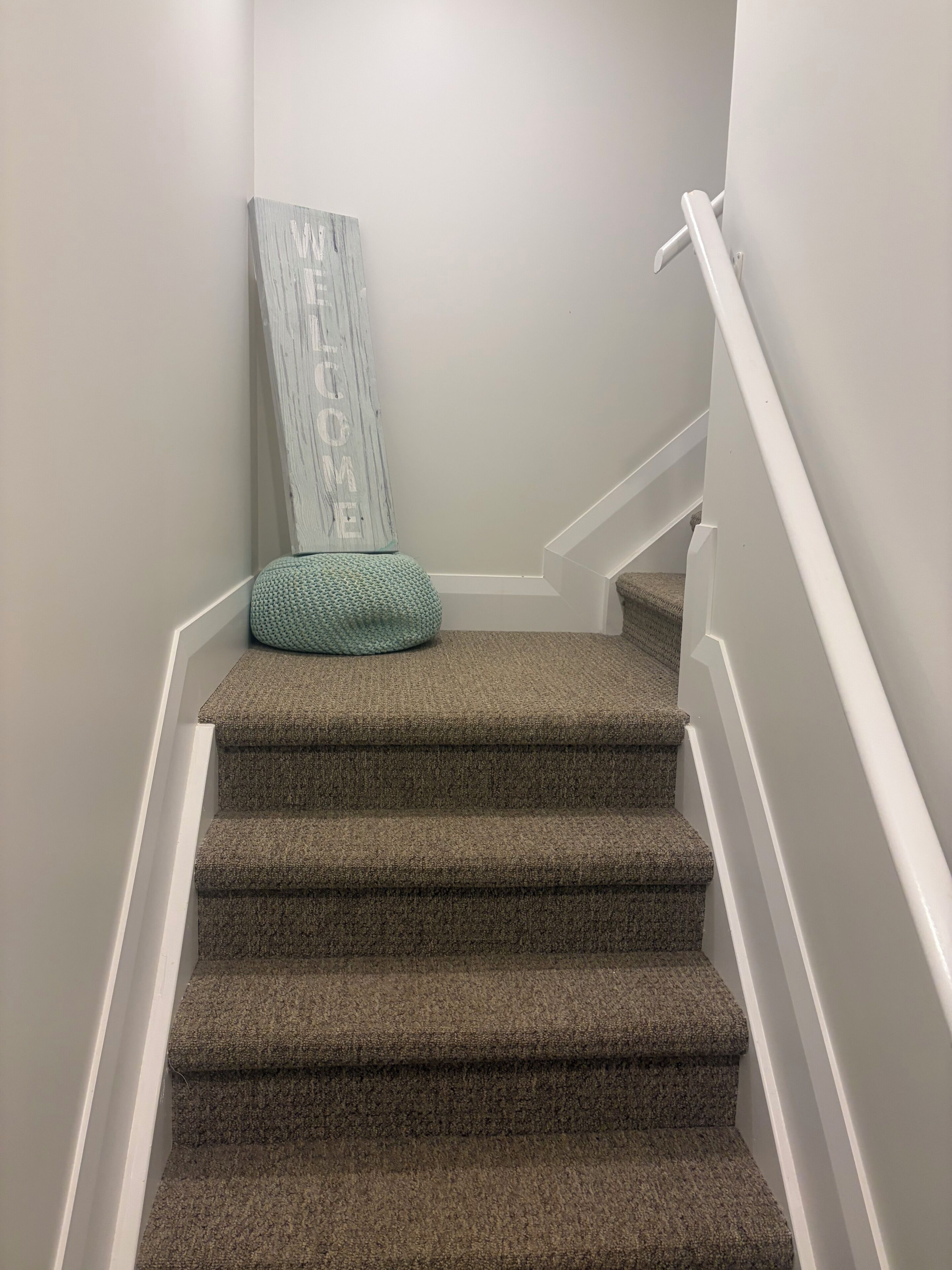 Una escalera alfombrada con barandilla blanca y felpudo en la parte inferior.