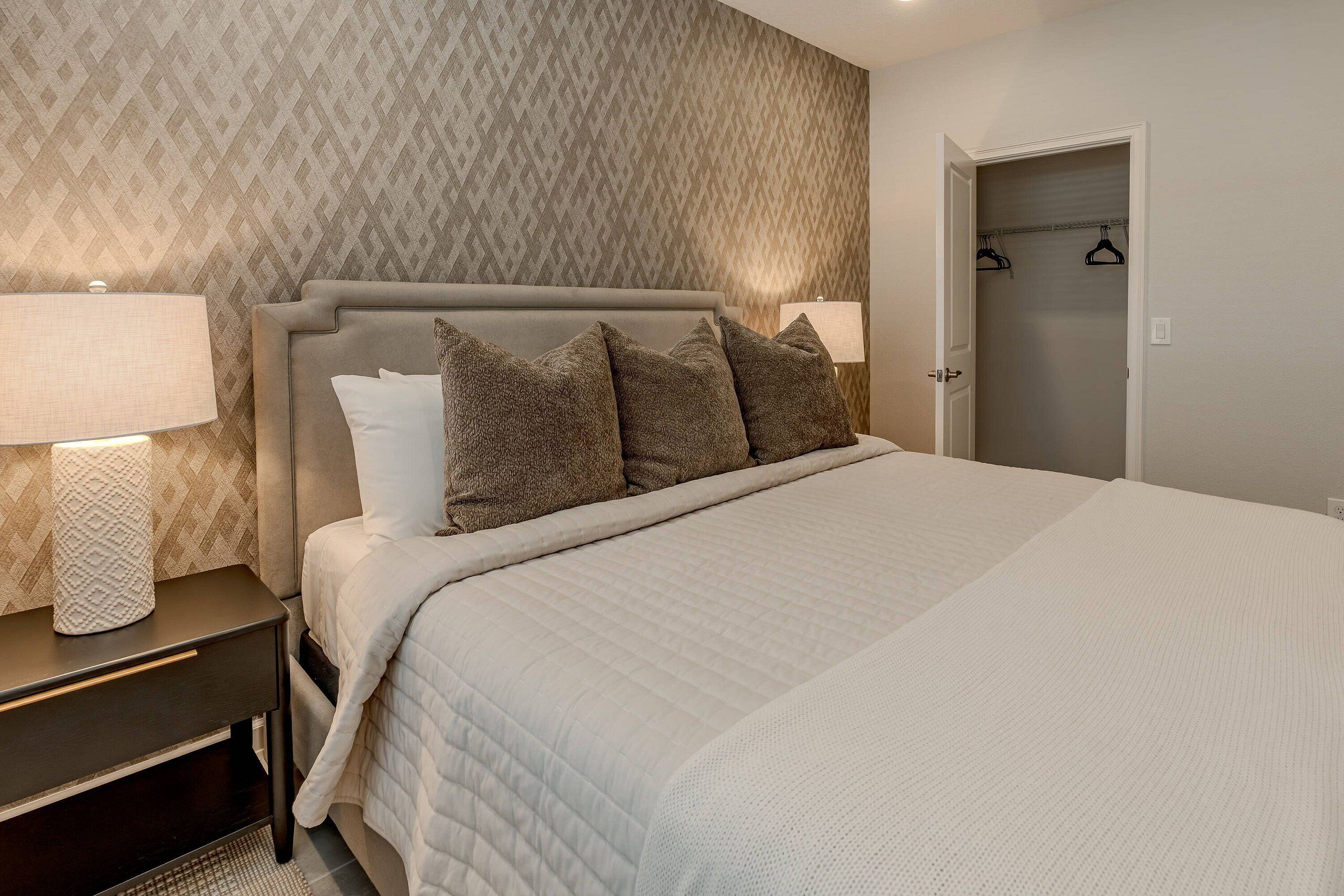 A neatly made bed with a headboard, two bedside lamps, and a patterned wallpaper.