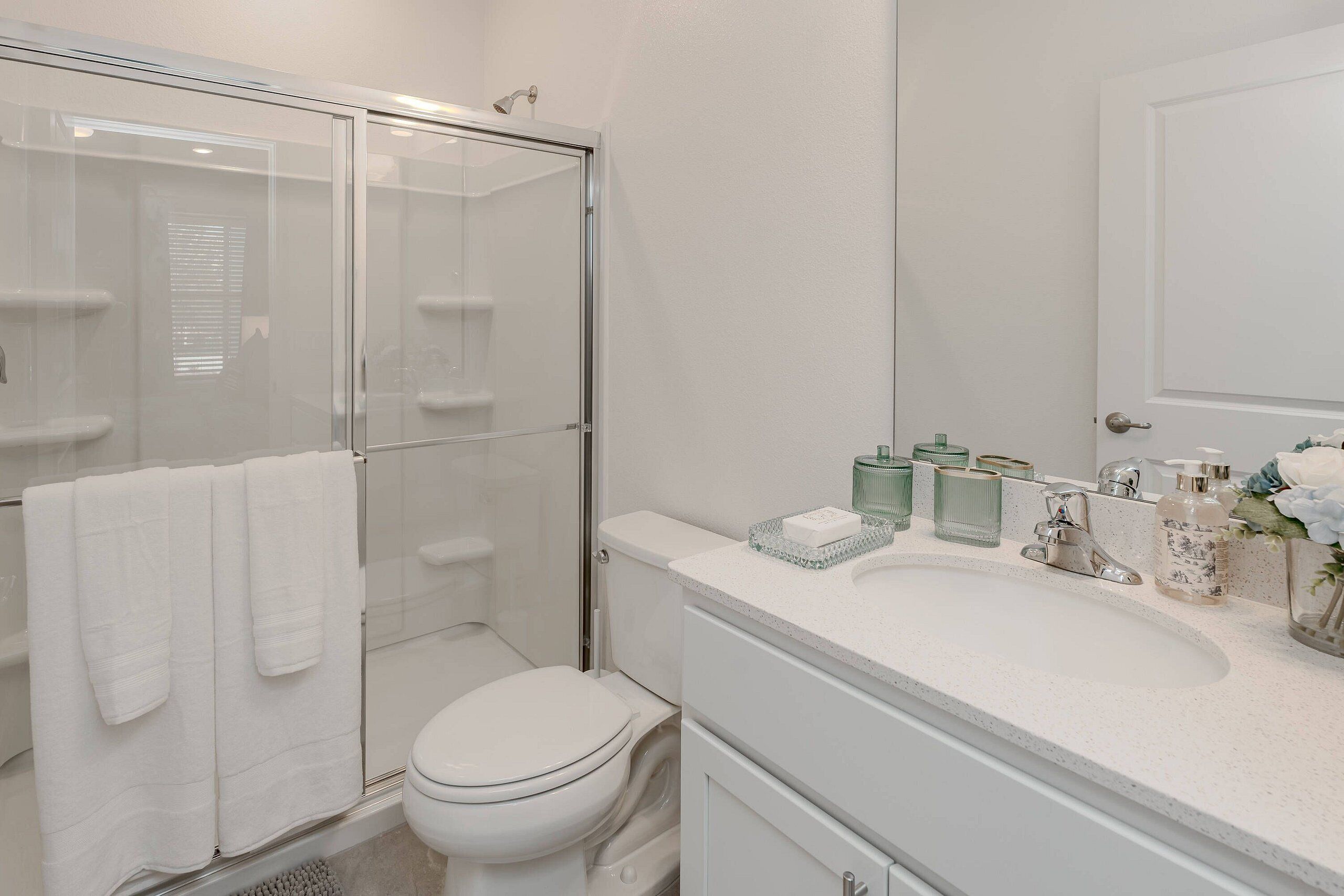 Une salle de bain moderne avec une douche à parois de verre, des toilettes blanches et un plan de toilette avec des articles de toilette.