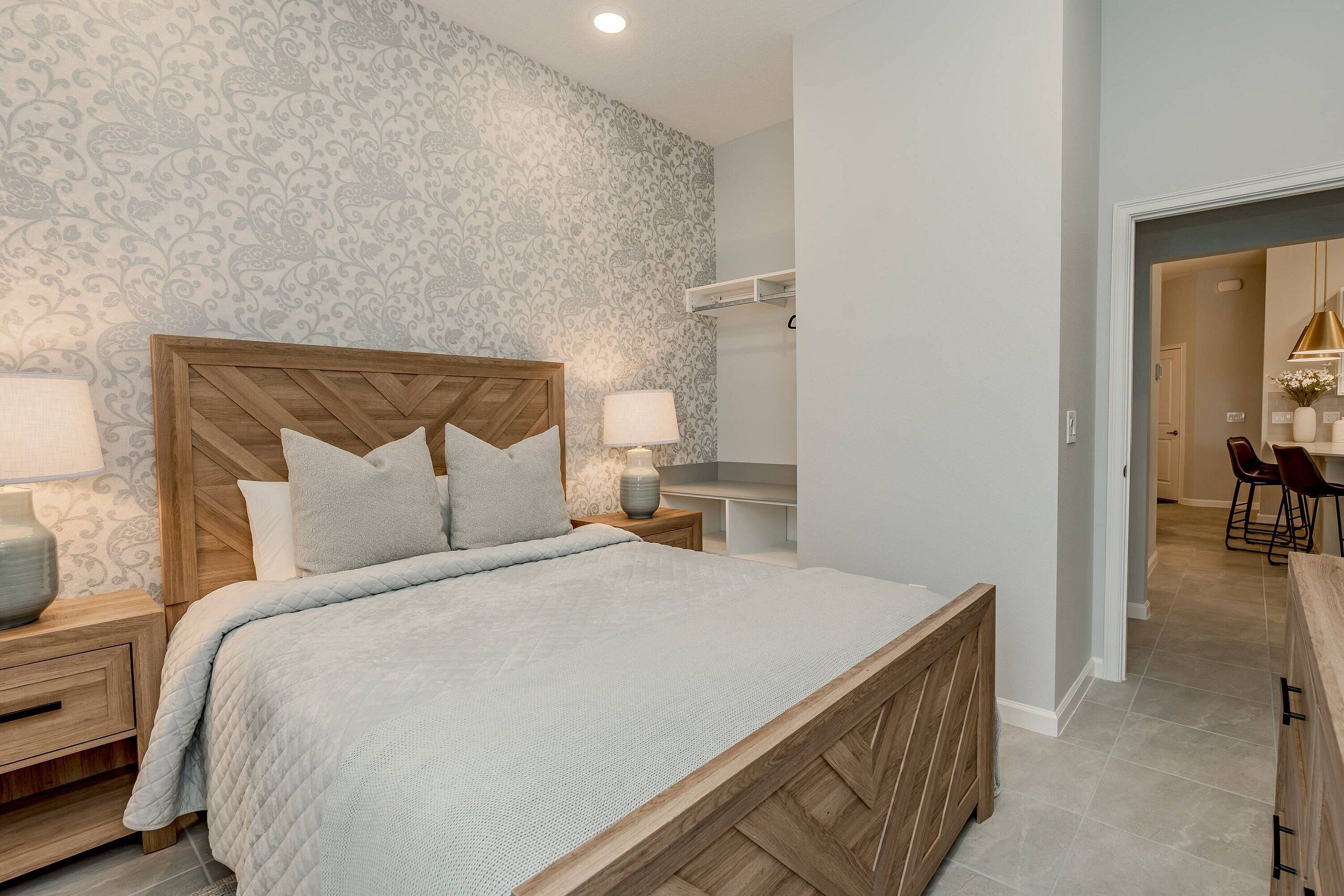 Une chambre à coucher avec une tête de lit en bois, un lit recouvert d’une courtepointe, des tables de chevet avec des lampes et un papier peint à motifs.