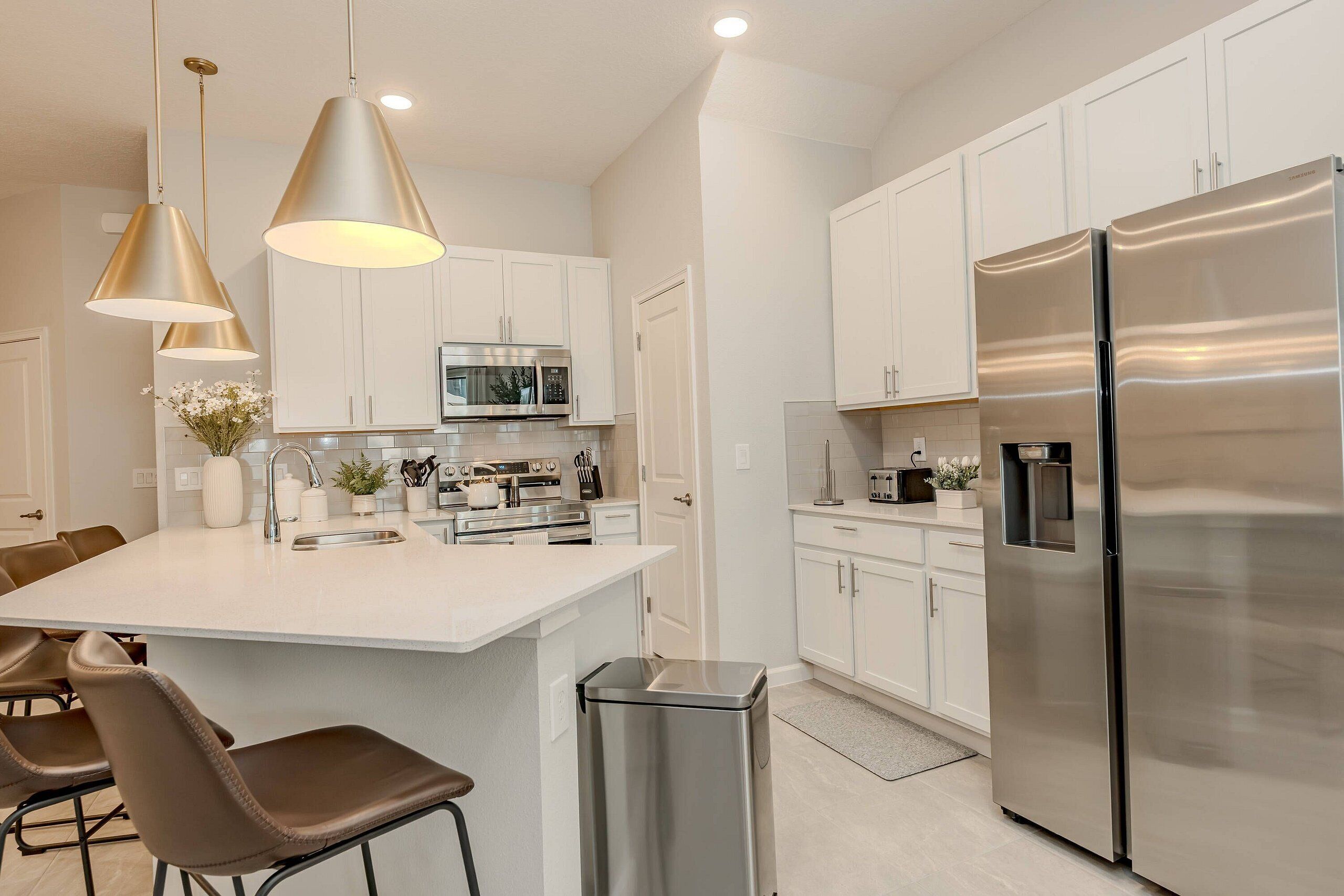 A modern kitchen with white cabinets, stainless steel appliances, and pendant lighting.