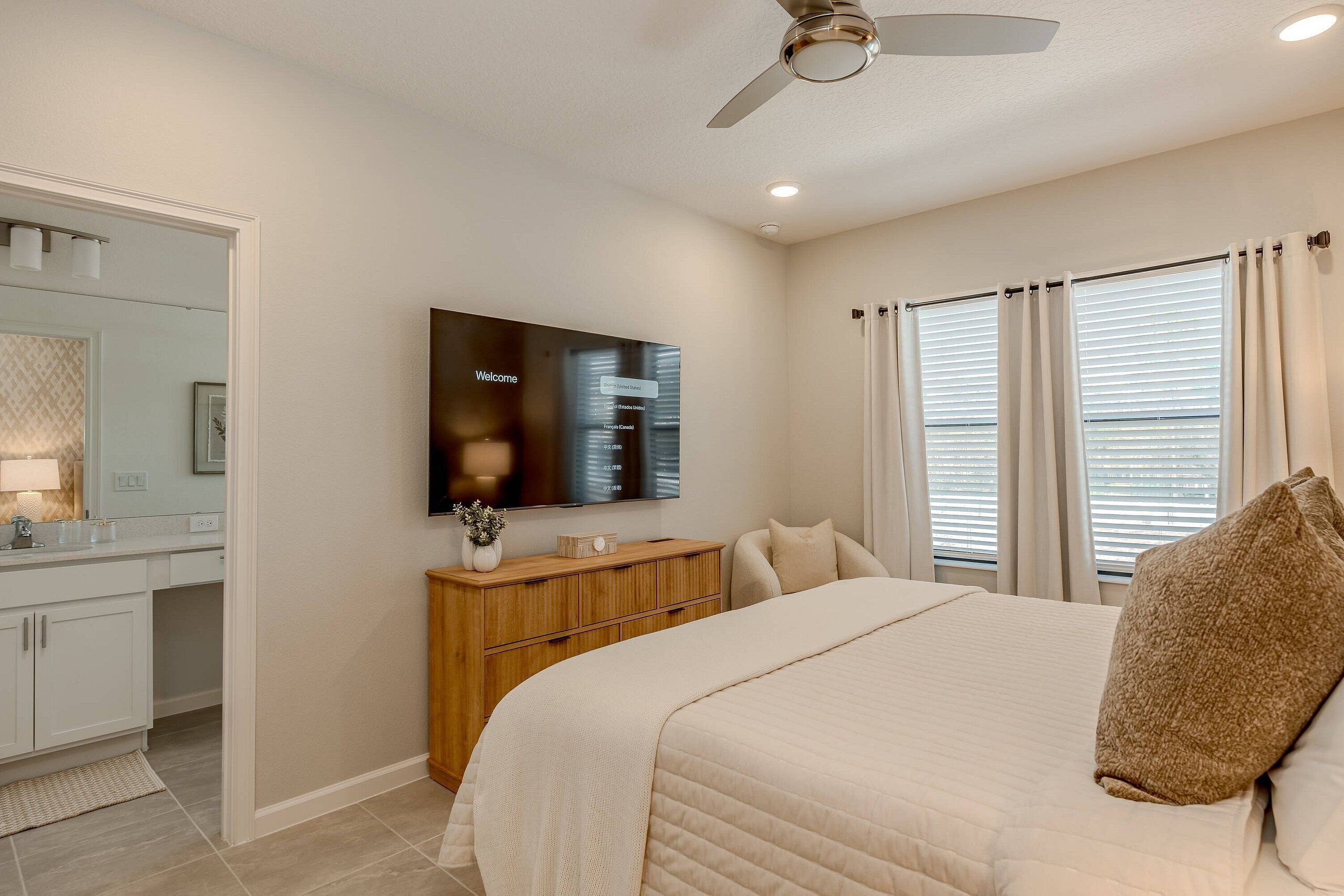 A bedroom with a bed, a TV, a wooden dresser, and a ceiling fan.