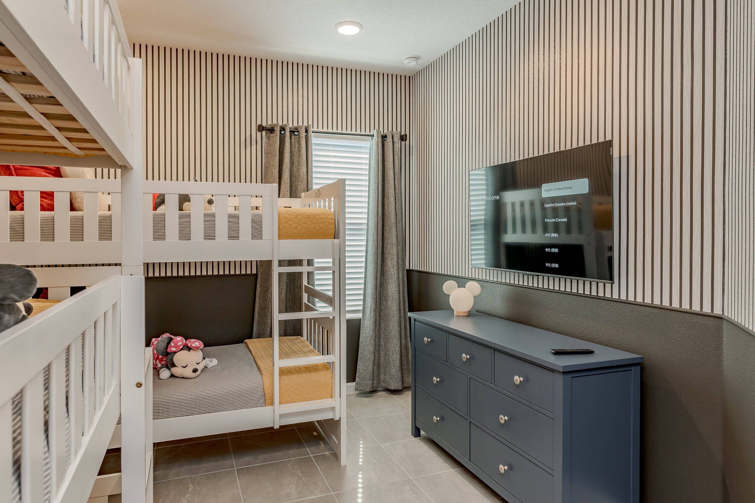 A child's bunk bed with a plush toy, a dark-colored dresser, and a television on the wall.