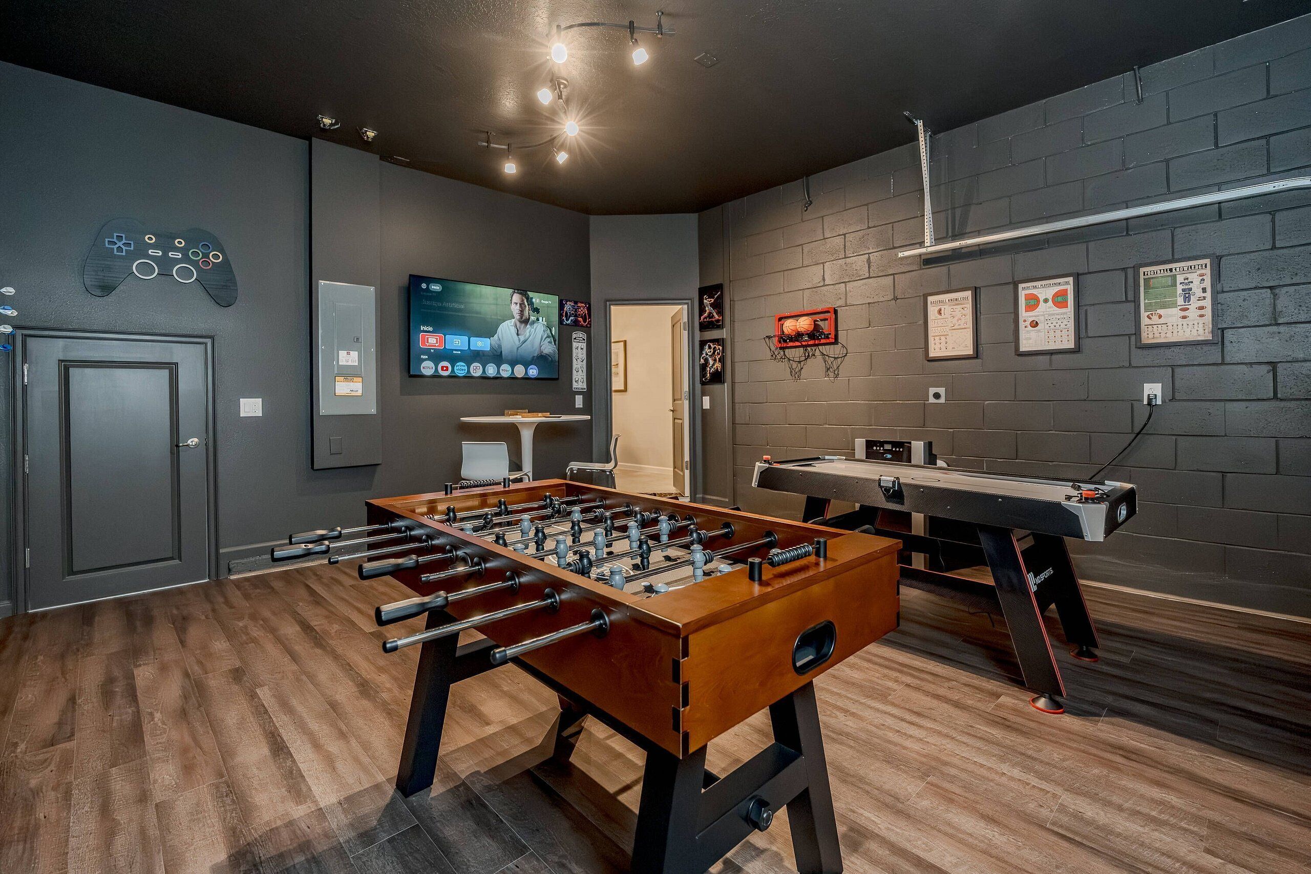A room with a foosball table, a pool table, and a television screen displaying a video game.