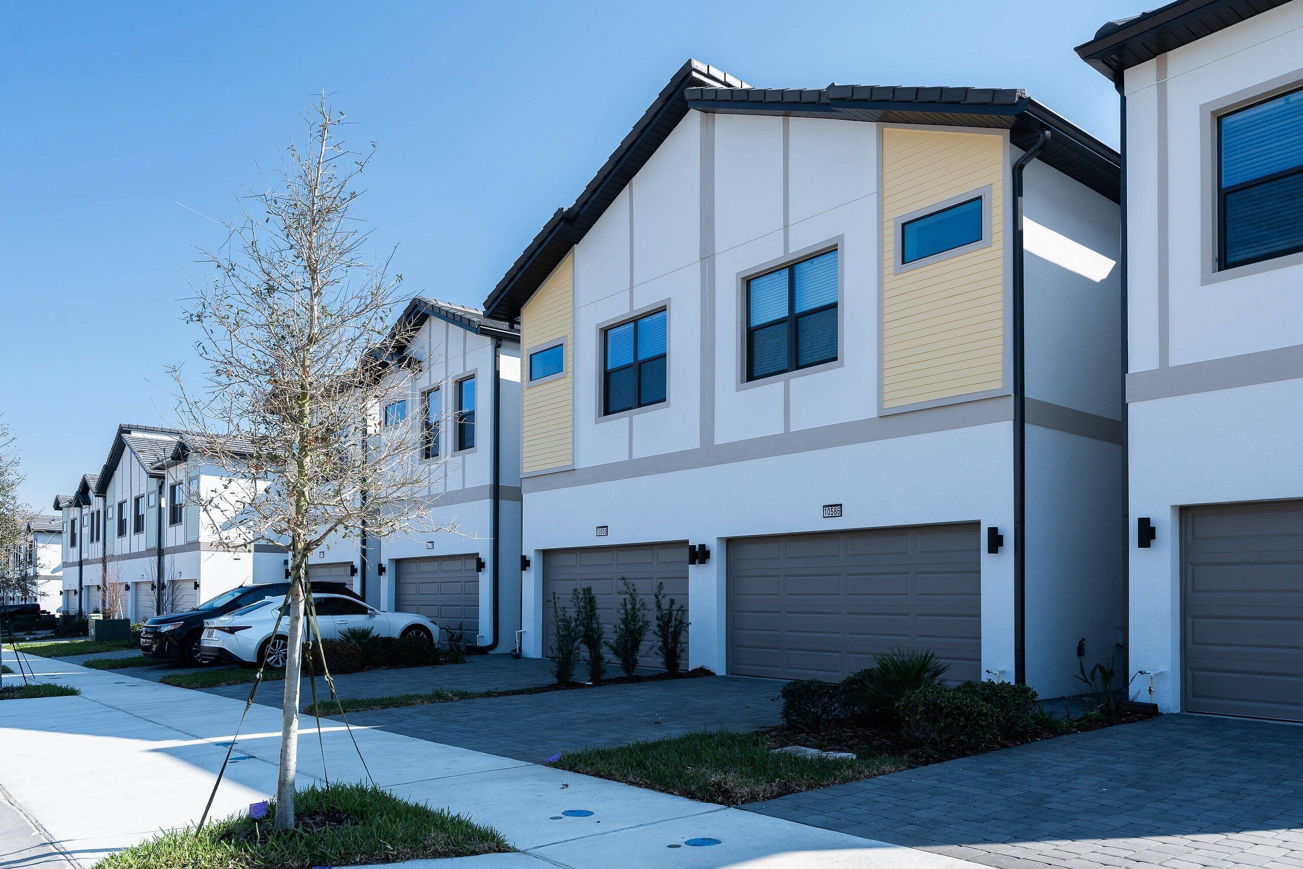 A modern residential building with multiple garage doors, a clear sky, and a tree in the foreground.