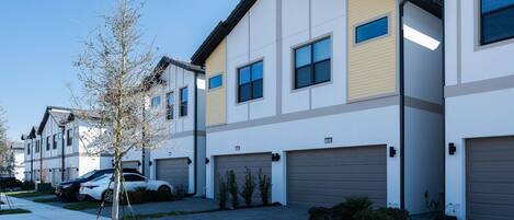 A modern residential building with multiple garage doors, a clear sky, and a tree in the foreground.
