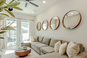A modern living room with a beige sectional sofa, a round coffee table, and three wall-mounted mirrors. - 5BR Home for 16 w/ Pool & Game Room (Orlando)