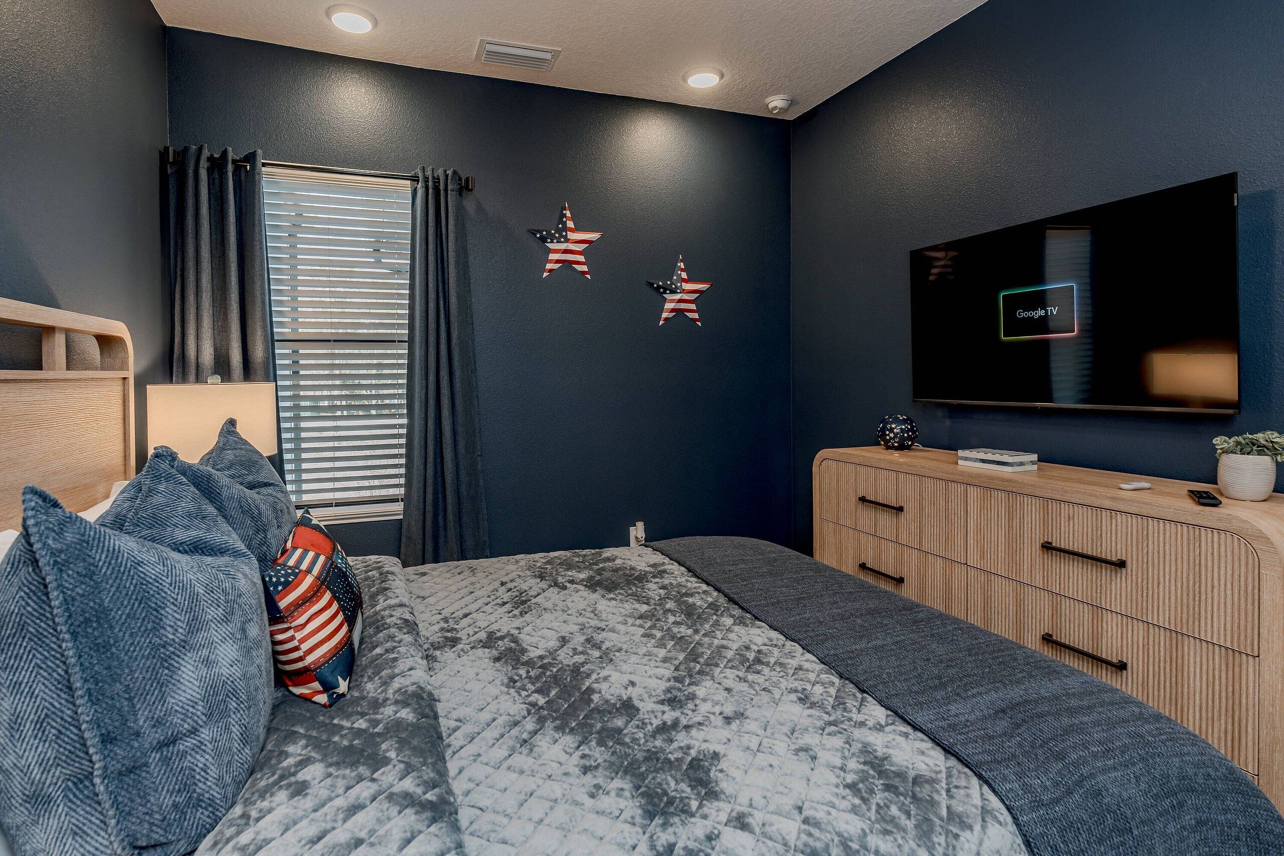 A bedroom with a bed, a dresser, a TV, and two American flag decorations on the wall.