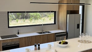 A modern kitchen with a large window, a built-in oven, a dishwasher, and a refrigerator. - Modern Luxe Bush Retreat | 3BR Near Trails (Nannup)