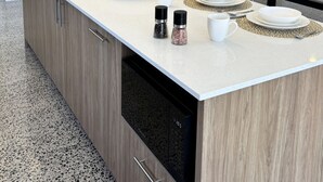 A modern kitchen with a built-in dishwasher, a fruit bowl, salt and pepper shakers, and a dining set. - Modern Luxe Bush Retreat | 3BR Near Trails (Nannup)